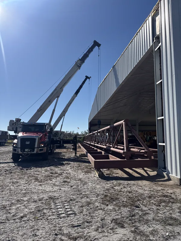 Two boom trucks staging a roof truss outside a finished hangar