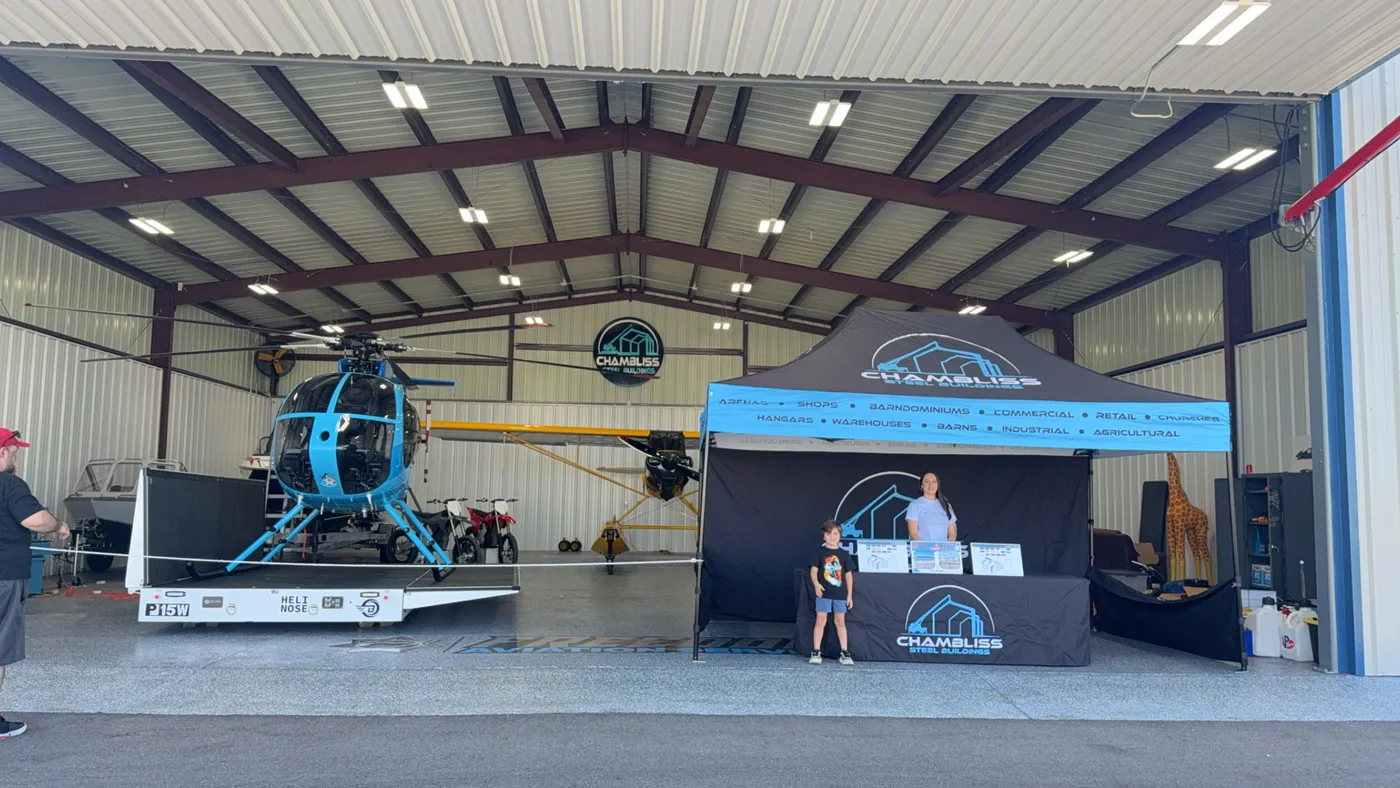 The Chambliss Steel Buildings booth set up inside a steel aircraft hangar, with a helicopter and a light aircraft parked alongside