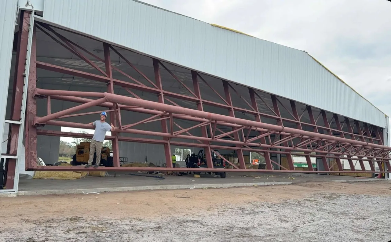 Bi-fold hangar door frame swung open, a worker standing on it for scale