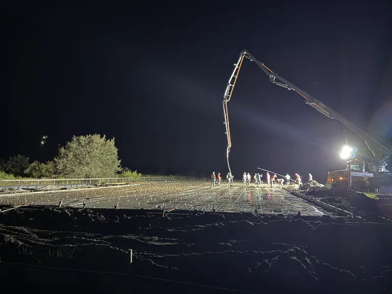 Night concrete pour, crew finishing a floodlit slab over rebar