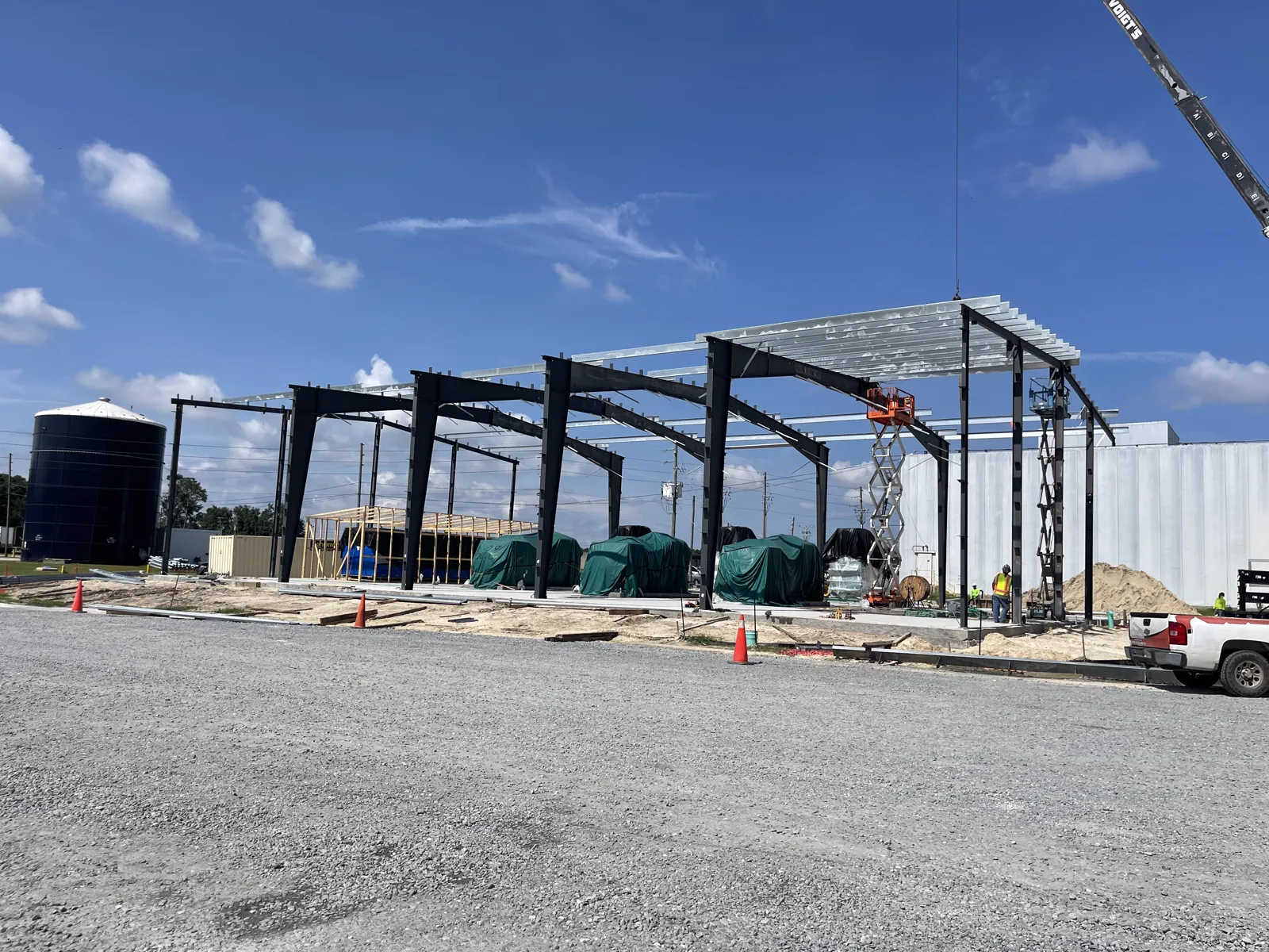 Crew and lift equipment working a steel frame alongside a finished concrete building