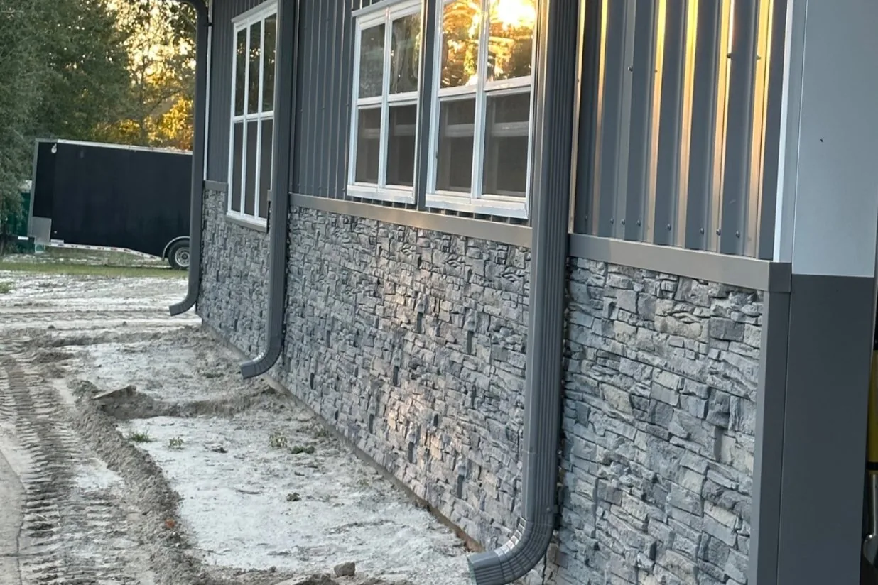Charcoal ribbed steel sidewall over gray stacked-stone wainscot at dusk