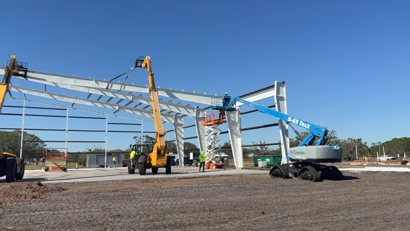 Crew setting steel columns and rafters with a telehandler and boom lift